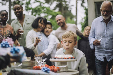 Junge bläst Kerze auf Kuchen während Geburtstagsfeier mit Familie - MASF32258