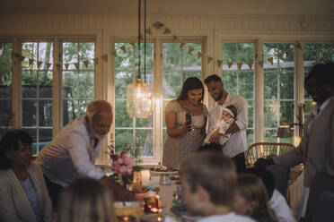 Glückliche Mutter zeigt ihrer Tochter, die vom Vater gehalten wird, das Smartphone während einer Dinnerparty zu Hause - MASF32281