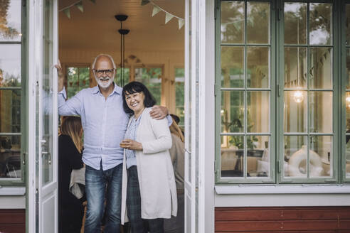 Portrait of happy senior man with arm around woman standing at doorway - MASF32287