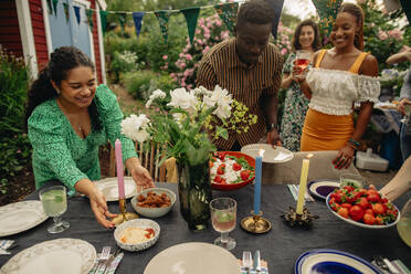 Male and female friends setting up table during garden party - MASF32299