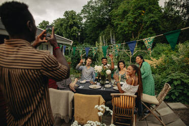 Man photographing male and female friends through smart phone at garden party - MASF32300