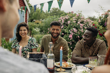 Man laughing while sitting at table with male and female friends during party - MASF32304