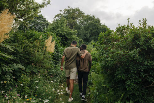 Rear view of male friends walking and talking in garden - MASF32309