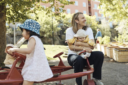 Glücklicher Vater, der wegschaut, während er mit seiner Tochter im Kindergarten sitzt und sich freut - MASF32350