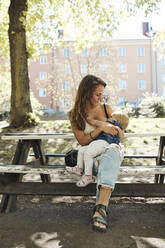 Mother breastfeeding toddler daughter while sitting on bench - MASF32354