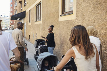 Smiling woman gesturing and talking to friends with baby stroller on sidewalk - MASF32369