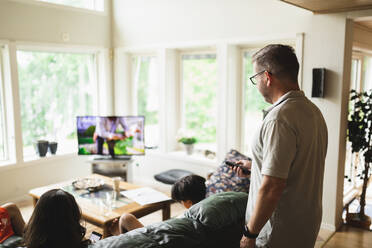 Vater wechselt den Fernsehkanal mit der Fernbedienung, während er zu Hause im Wohnzimmer steht - MASF32384