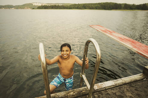 Hohe Winkelansicht des hemdlosen Jungen hält Geländer in See im Urlaub - MASF32385