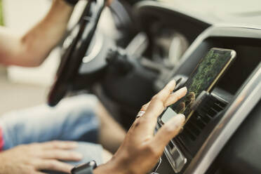 Hand of woman using GPS through smart phone attached on dashboard in car - MASF32387