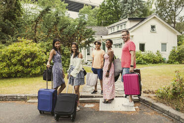 Portrait of happy multiracial family standing with luggage in front of house - MASF32390