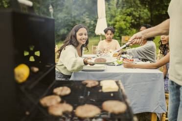 Mittelteil eines Vaters, der einer lächelnden Tochter, die auf einem Tisch im Hinterhof sitzt, eine gegrillte Pastete serviert - MASF32394