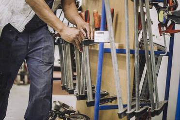 Male carpenter arranging work tools on rack while working in workshop - MASF32434