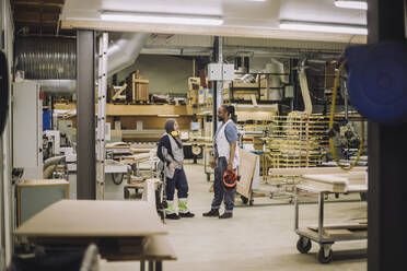 Full length of male and female carpenters discussing while standing in warehouse - MASF32435