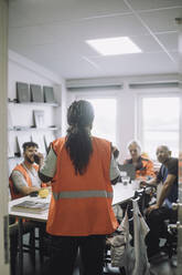 Rückansicht eines Schreiners, der mit Kollegen in einem Lagerbüro während einer Besprechung diskutiert - MASF32452