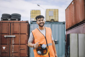 Porträt eines glücklichen jungen Bauarbeiters mit Schutzhelm auf der Baustelle - MASF32473