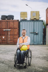 Portrait of smiling construction worker sitting in wheelchair at site - MASF32475