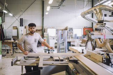 Portrait of young carpenter standing by machinery in workshop - MASF32516