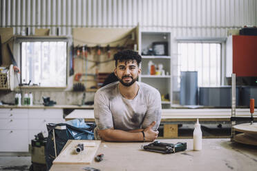 Portrait of smiling carpenter leaning on workbench - MASF32517