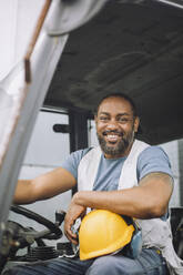 Porträt eines glücklichen reifen Bauarbeiters mit Schutzhelm, der in einem Fahrzeug sitzt - MASF32568