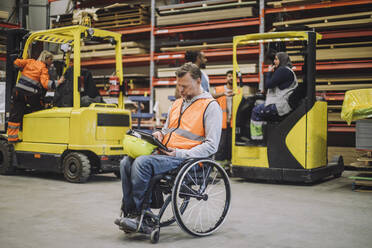 Full length of male carpenter with disability using digital tablet sitting on wheelchair in warehouse - MASF32597