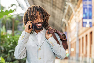 Happy businessman talking on mobile phone at station - DLTSF03123