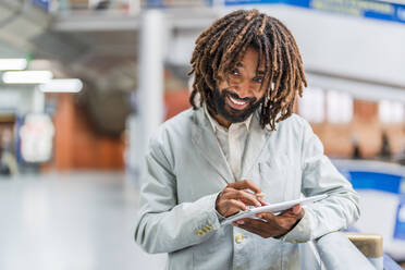 Happy businessman holding tablet PC at central station - DLTSF03133