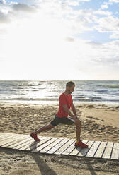 Man doing stretching exercise on boardwalk at beach - VEGF06065