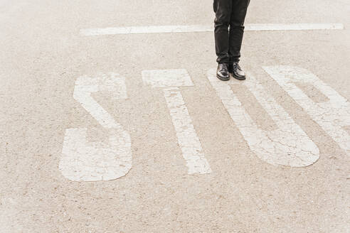 Beine eines Mannes auf einem STOP-Schild an der Straße - MGRF00820