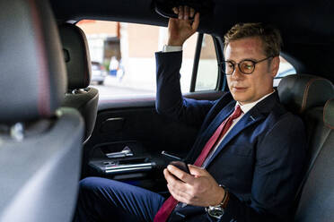 Businessman using smart phone sitting in car - DLTSF03144
