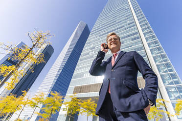 Smiling businessman talking on mobile phone in front of office building - DLTSF03156