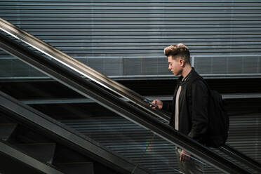 Young man using smart phone on escalator - EGAF02572