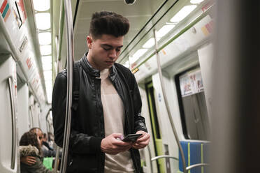 Young man using smart phone in subway train - EGAF02574