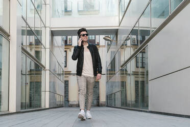 Lächelnder Mann mit Sonnenbrille, der inmitten eines Gebäudes mit seinem Mobiltelefon spricht - EGAF02578