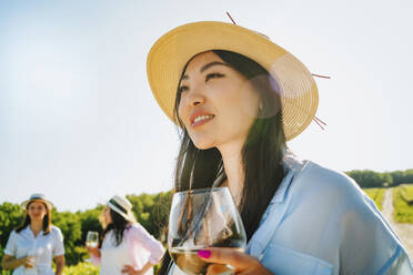 Lächelnde Frau mit Hut und Weinglas an einem sonnigen Tag - MDOF00025
