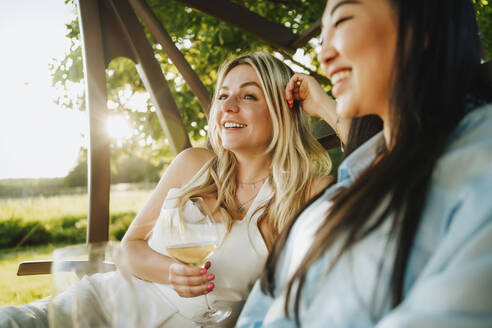 Happy friends holding white wine on porch swing at winery - MDOF00028