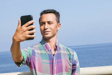 Lächelnder Mann nimmt Selfie durch Smartphone vor dem Meer - ACTF00275