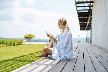 Frau mit Smartphone auf Veranda sitzend - MDOF00043
