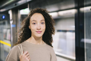 Lächelnde Frau mit lockigem Haar an einer U-Bahn-Station - AMWF00885