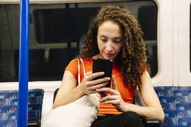 Junge Frau mit Mobiltelefon in der U-Bahn sitzend - AMWF00898