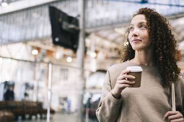Lächelnde Frau mit Einwegbecher Kaffee am Bahnhof - AMWF00912