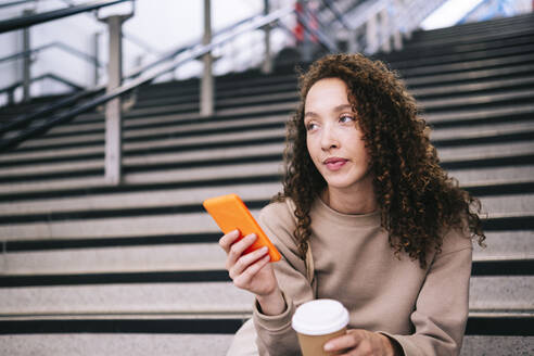 Young woman with mobile phone sitting on steps - AMWF00913