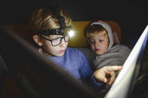 Junge mit Scheinwerfern, der mit seinem Bruder zu Hause ein Buch liest - EYAF02225