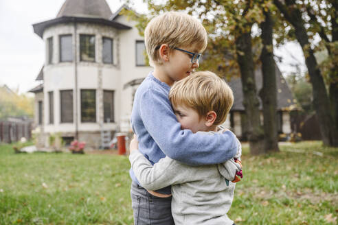 Siblings hugging each other in back yard - EYAF02239