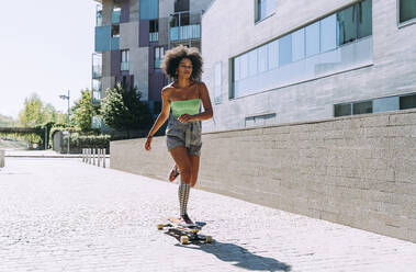 Junge Frau Longboard Skaten außerhalb Gebäude auf sonnigen Tag - OIPF02416