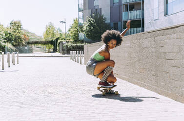 Young woman crouching on skateboard outside building - OIPF02417