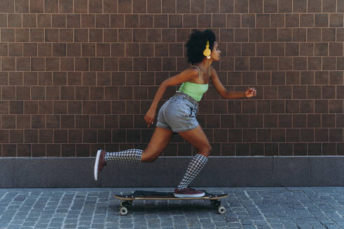 Woman longboard skating on footpath by wall - OIPF02421