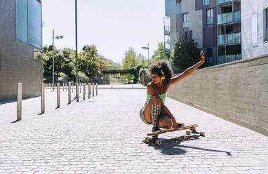 Woman crouching on skateboard outside building - OIPF02422