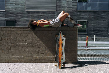 Frau an der Wand liegend mit Skateboard an einem sonnigen Tag - OIPF02426