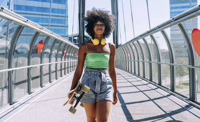 Junge Frau steht mit Skateboard auf einer Brücke - OIPF02428