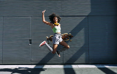 Unbekümmerte junge Frau mit Skateboard, die vor eine Wand springt - OIPF02432